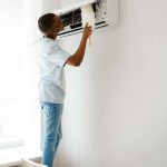 A man cleaning the filter of an air conditioning unit with a brush