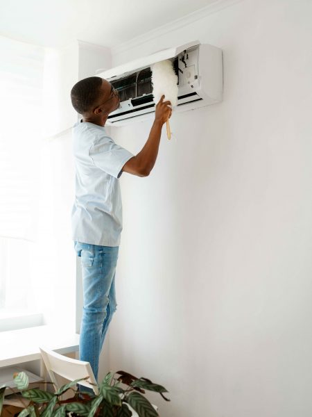 A man cleaning the filter of an air conditioning unit with a brush